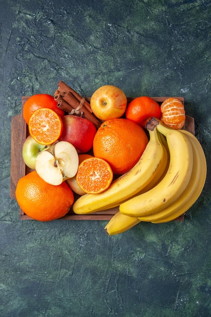 Vista superior frutas frescas naranjas mandarinas manzanas plátanos y palitos de canela en bandeja de madera sobre fondo oscuro espacio libre