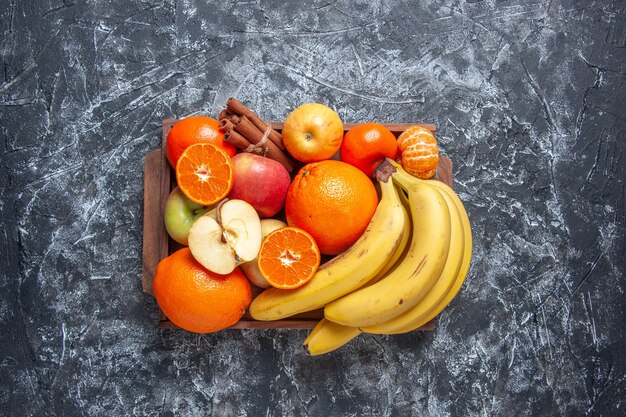 Vista superior frutas frescas plátanos manzanas naranjas canela en bandeja de madera en la mesa