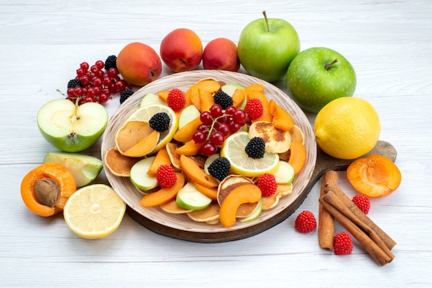 Una vista superior de frutas frescas en rodajas suaves con canela y frutas enteras en el escritorio de madera y comida de color de frutas de fondo blanco