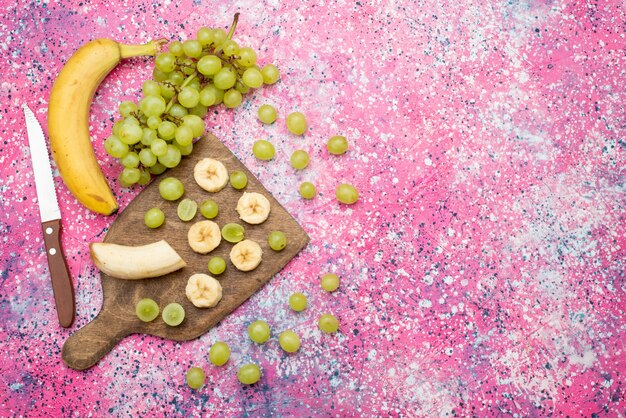 Vista superior de frutas frescas en rodajas, uvas frescas y plátanos en la superficie púrpura, color de jugo suave de frutas