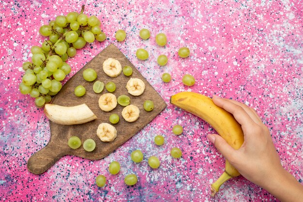 Vista superior de frutas frescas en rodajas, uvas y plátanos en el escritorio púrpura vitamina color de frutas