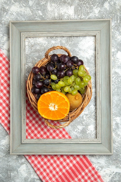 Vista superior de frutas frescas uvas y naranjas dentro de la cesta y el bastidor en la superficie blanca fruta madura vitamina fresca suave