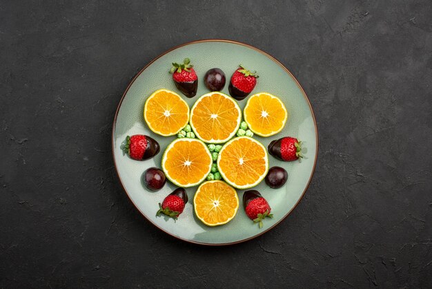 Vista superior de frutas lejanas y naranja picada de chocolate con fresas cubiertas de chocolate y caramelos verdes en la mesa oscura