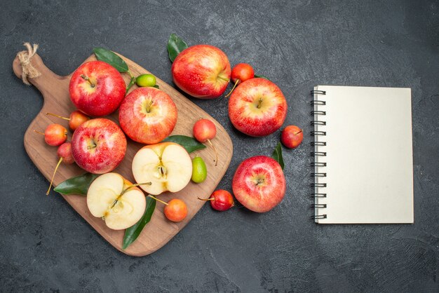 Vista superior de frutas manzanas rojas-amarillas y cerezas en el tablero junto al cuaderno de manzanas