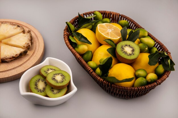 Vista superior de frutas orgánicas como kiwi kinkans y limones en un balde con rodajas de kiwi en un recipiente sobre un fondo gris