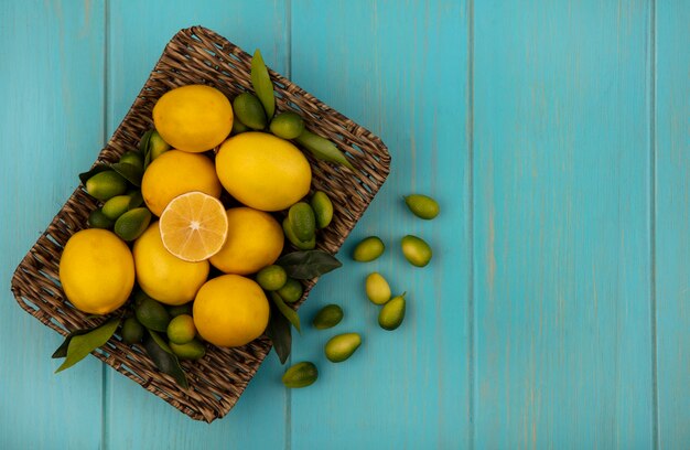 Vista superior de frutas saludables como kinkans y limones en una bandeja de mimbre sobre un fondo de madera azul con espacio de copia