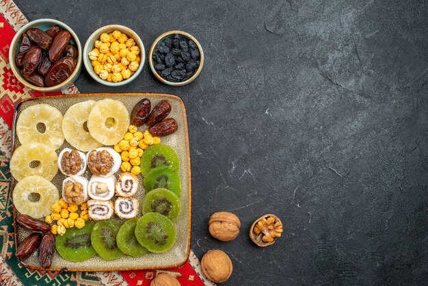 Vista superior de frutas secas en rodajas, anillos de piña y kiwis sobre fondo gris, frutos secos, pasas, vitamina dulce, vitamina agria, salud