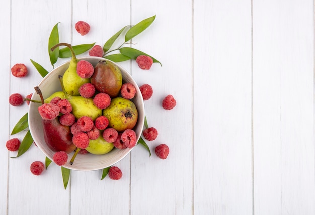 Vista superior de frutas en un tazón con hojas sobre superficie de madera