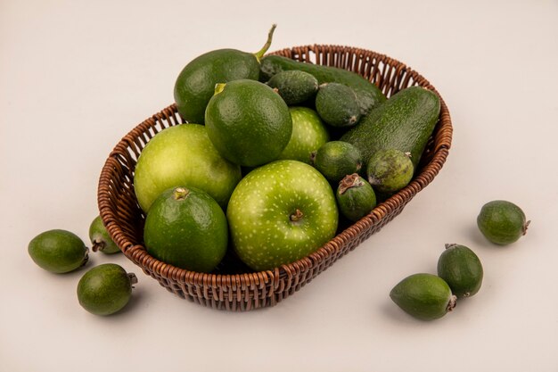 Vista superior de frutas verdes saludables como manzanas, aguacates, limas y feijoas en un balde sobre una pared blanca