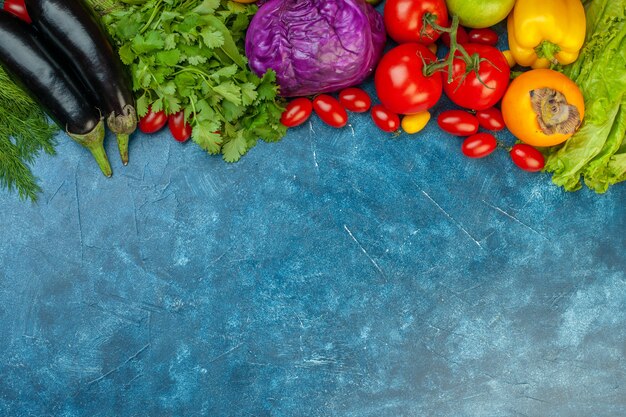 Vista superior de frutas y verduras, tomates cherry, pimientos, tomates, repollo rojo, cilantro, berenjenas en el espacio libre de la mesa azul