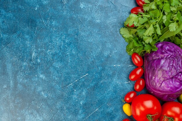 Vista superior de frutas y verduras, tomates cherry, tomates cumcuat, repollo rojo, cilantro en mesa azul