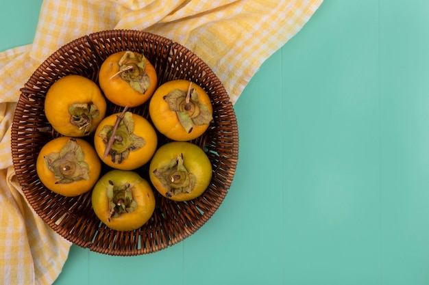 Foto gratuita vista superior de frutos de caqui inmaduros de color naranja en un balde sobre un paño amarillo marcada