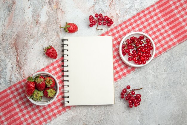 Vista superior de frutos rojos con bayas en un bloc de notas de bayas de frutas frescas de mesa blanca