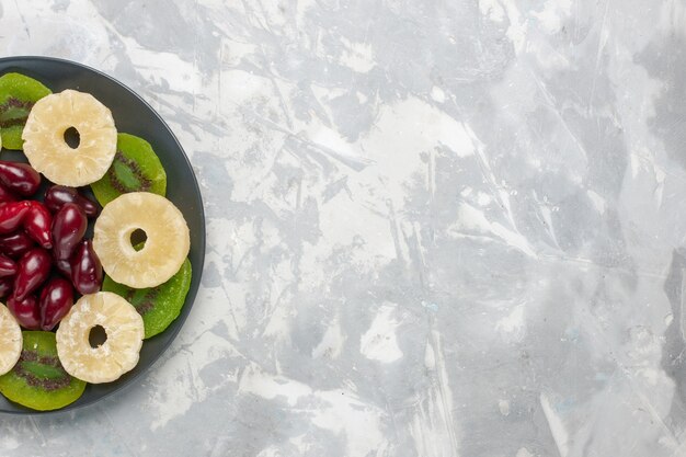 Vista superior de frutos secos, anillos de piña y rodajas de kiwi en el escritorio blanco, fruta seca, azúcar dulce, agria