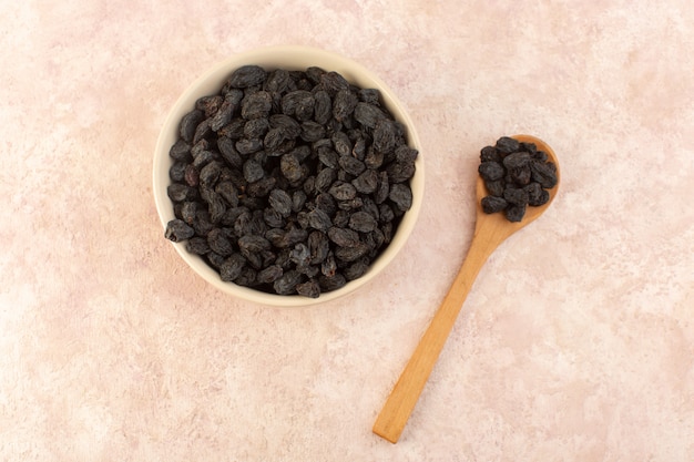 Una vista superior de frutos secos negros dentro de un plato redondo con cuchara de madera en rosa