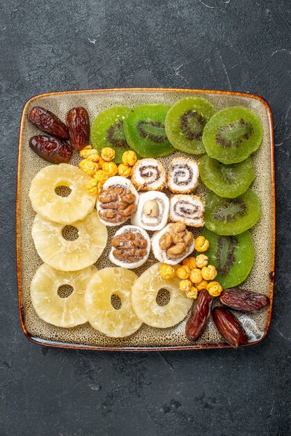 Vista superior de frutos secos en rodajas, anillos de piña y kiwis sobre el fondo gris, frutos secos, pasas, vitamina agridulce, salud