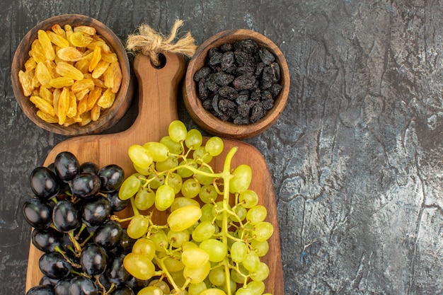 Foto gratuita vista superior de frutos secos uvas en la tabla de madera entre dos tazones de frutos secos