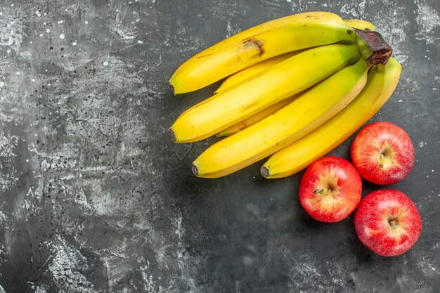 Vista superior de la fuente de nutrición orgánica paquete de bananas frescas y manzanas rojas en el lado izquierdo sobre fondo oscuro
