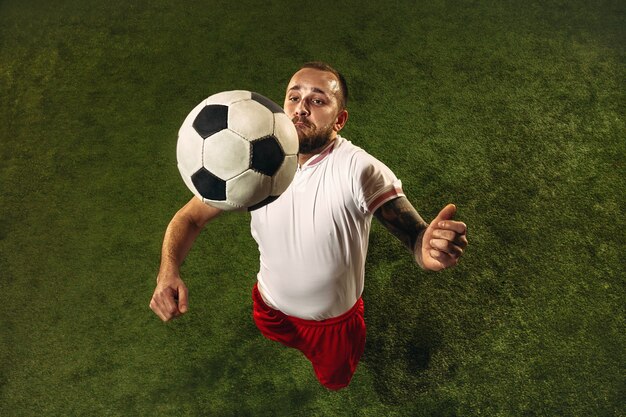 Vista superior del fútbol caucásico o jugador de fútbol sobre fondo verde de hierba. Entrenamiento modelo deportivo masculino joven, practicando. Patear la pelota, atacar, atrapar. Concepto de deporte, competición, ganar.