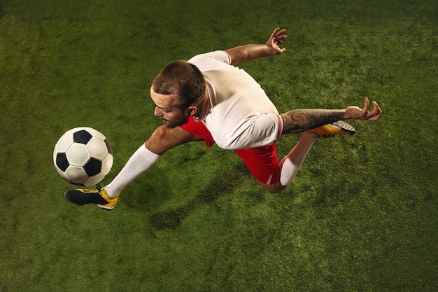 Vista superior del fútbol caucásico o jugador de fútbol sobre fondo verde de hierba. Entrenamiento modelo deportivo masculino joven, practicando. Patear la pelota, atacar, atrapar. Concepto de deporte, competición, ganar.