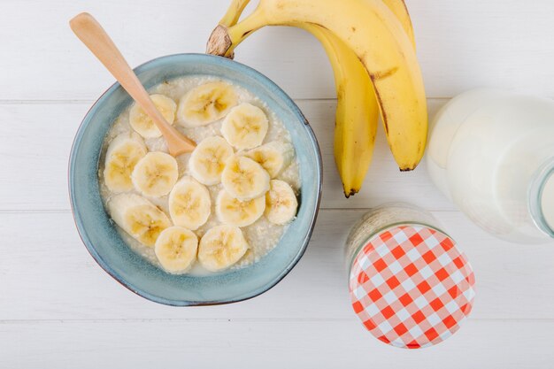 Vista superior de gachas de avena con plátano en un tazón de cerámica en la mesa rústica