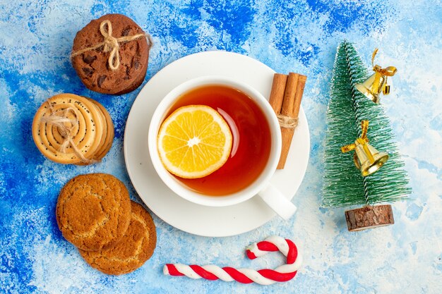 Vista superior de las galletas atadas con una cuerda taza de té pequeño árbol de Navidad en la mesa azul