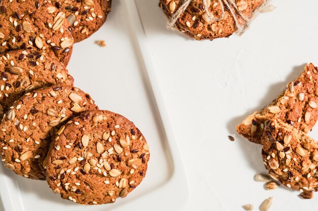 Vista superior de galletas de avena caseras con semillas de lino y sésamo sobre una mesa blanca. Concepto de comida sana fitness. Leche y galletas, desayuno saludable. Diseño de galletas de Navidad en un plato