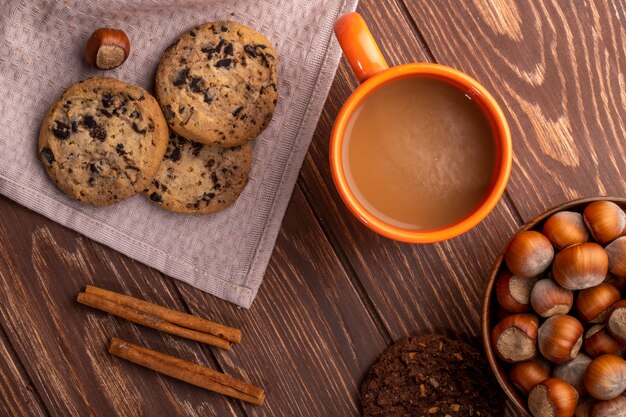 Vista superior de galletas de avena con chispas de chocolate y cacao y una taza con bebida de cacao en madera