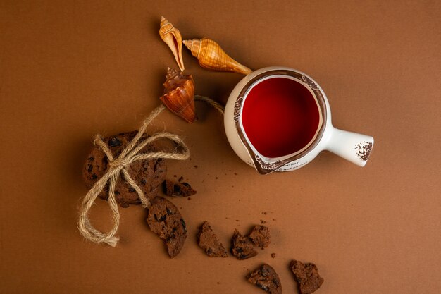 Vista superior de galletas de avena con chispas de chocolate cayendo conchas rotas y una taza de té en ocre