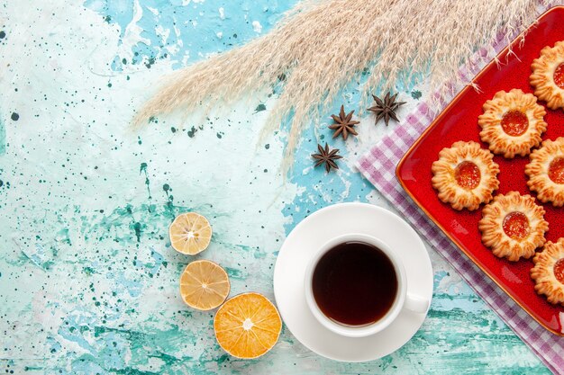 Vista superior de las galletas de azúcar dentro de la placa roja con una taza de té sobre el fondo azul.