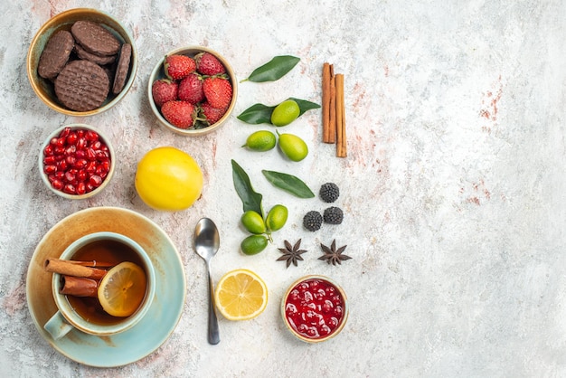 Vista superior galletas y bayas apetitosas galletas fresas cuchara una taza de té frutas cítricas canela sobre la mesa