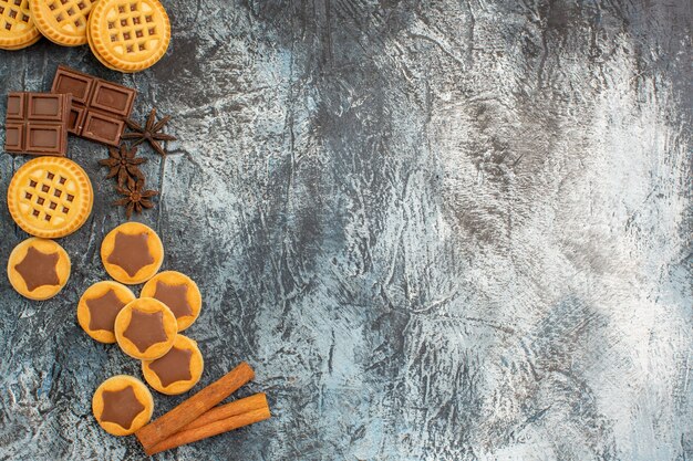 Vista superior de galletas con canela y chocolates en el lado izquierdo de la tierra gris