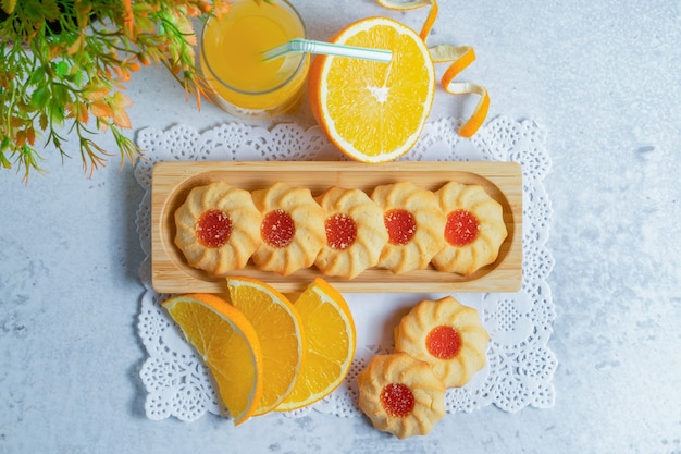 Vista superior de galletas caseras frescas con mermelada y rodajas de naranja en la pared gris.