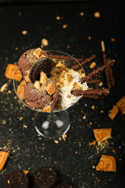 Vista superior de galletas con chispas de chocolate con crema batida y palitos de chocolate en vidrio sobre mesa negra