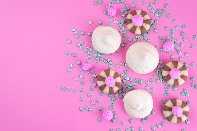 Una vista superior de las galletas de chocolate deliciosas y deliciosas con merengues en el escritorio rosa, caramelo de color galleta de galleta