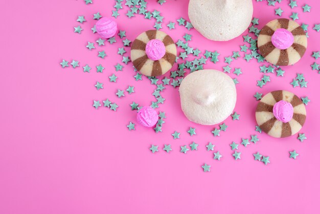 Una vista superior de las galletas de chocolate junto con merengues en el escritorio rosa, galleta de galleta de azúcar dulce