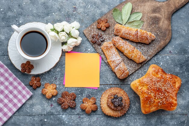 Vista superior galletas deliciosas dulces con taza de café y brazaletes dulces de pastelería el café dulce azúcar de galletas de mesa gris