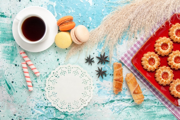 Vista superior de galletas dulces con bagels de mermelada de naranja y una taza de té sobre el fondo azul.