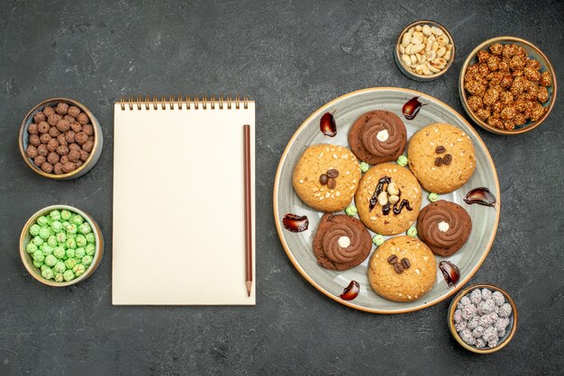 Vista superior de las galletas dulces con caramelos en el piso de color gris oscuro, galletas de azúcar, galletas dulces, té