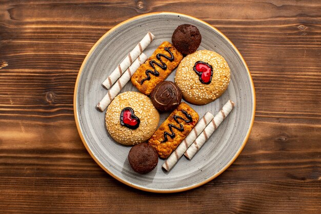 Vista superior galletas dulces deliciosos dulces dentro de la placa sobre fondo marrón rústico té galleta galleta azúcar dulce