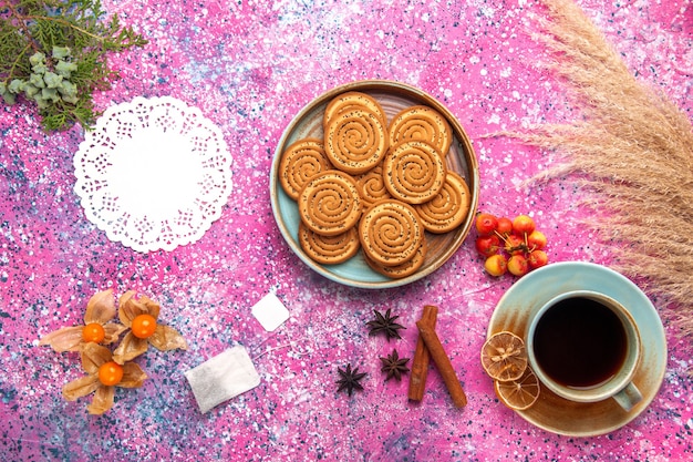 Vista superior de galletas dulces dentro de la placa con canela y taza de té en la superficie rosa