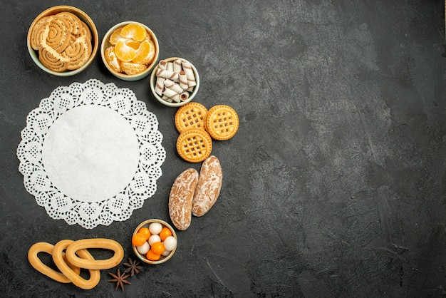 Vista superior de galletas dulces con frutas y caramelos en el piso oscuro