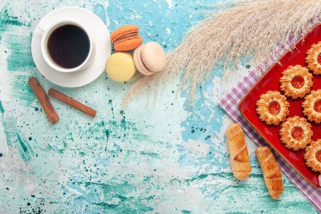 Vista superior de galletas dulces con macarons de bagels y taza de té sobre fondo azul claro