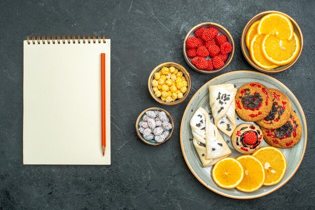 Vista superior de galletas dulces con pasteles, rodajas de naranja y caramelos en la superficie oscura de la torta de galletas dulces de galletas de té