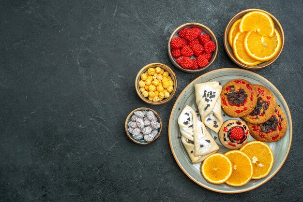 Vista superior de galletas dulces con pasteles, rodajas de naranja y caramelos en la superficie oscura de la torta de galletas dulces de galletas de té