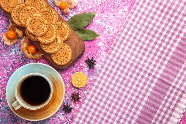 Vista superior de galletas dulces redondas con taza de té en la superficie rosa