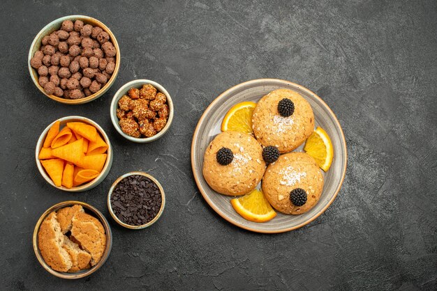 Vista superior de las galletas dulces con rodajas de naranja y patatas fritas en el té dulce de la galleta de la galleta del refrigerio backgruond gris oscuro