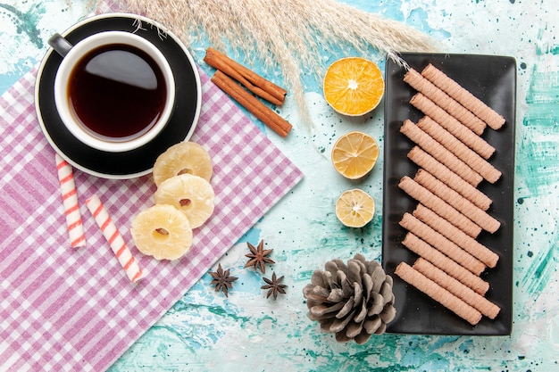 Vista superior de galletas dulces con taza de té y anillos de piña secos sobre fondo azul.