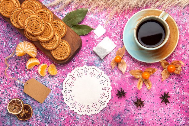 Vista superior de galletas dulces con taza de té y mandarinas en la superficie rosa