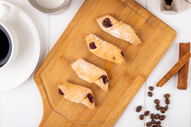 Vista superior de las galletas de harina con mermelada de fresa sobre una plancha de madera sobre fondo blanco.